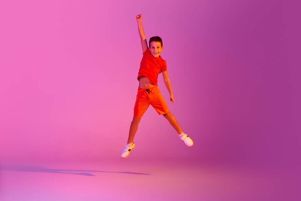 In flight. Emotional kid in casual bright clothes jumping isolated over pink background in neon. Kids emotions, news, challenges, childhood, education concept. Copy space for ad