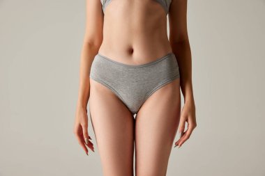 Gri stüdyo arka planında izole edilmiş ince kadın vücudu, göbek ve kalçasının görüntüsü. Vücut şekli. Güzellik, vücut ve cilt bakımı, sağlık, estetik cerrahi, kozmetik