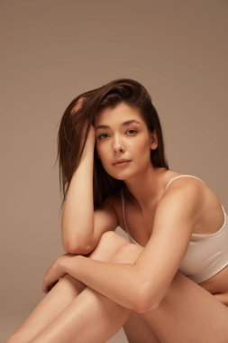 İç çamaşırlarıyla poz veren güzel bir kadının portresi koyu bej renkli bir arka plan üzerine izole edilmiş. Kadınlık. Kendini sevme. Güzellik, vücut ve cilt bakımı, sağlık, estetik cerrahi, kozmetik