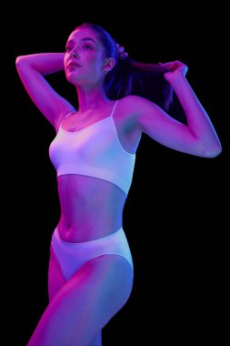 Beyaz iç çamaşırlarıyla poz veren güzel bir kadının portresi. Siyah arka planda, neon ışıkta izole edilmiş. Mükemmel vücut şekli. Güzellik, vücut ve cilt bakımı, sağlık, estetik cerrahi, kozmetik