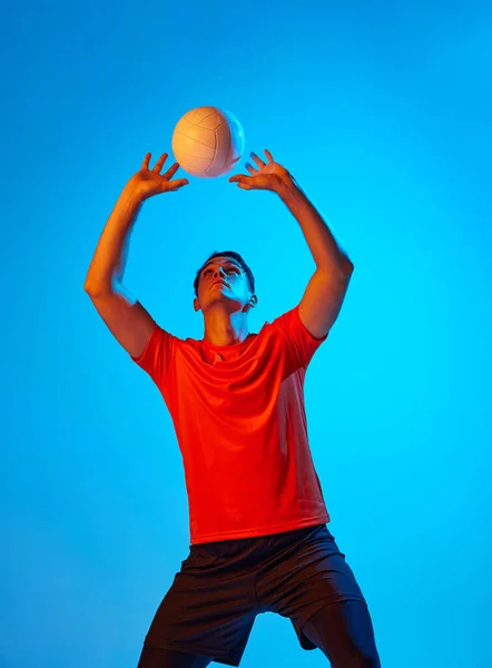 一名身穿橙色 黑色制服训练的男子排球运动员 在霓虹灯下的蓝色工作室背景上与球隔离 团队运动 打排球的运动员 — 图库照片