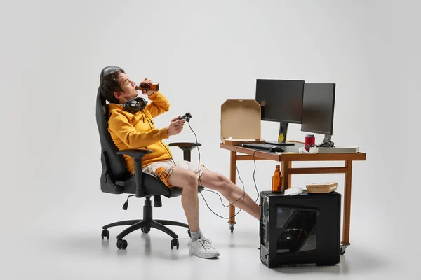 Leisure activity. Lazy man, student sitting at home, playing computer games isolated over grey background. Business, studying, education, youth, remote workplace concept. Copy space for ad, text