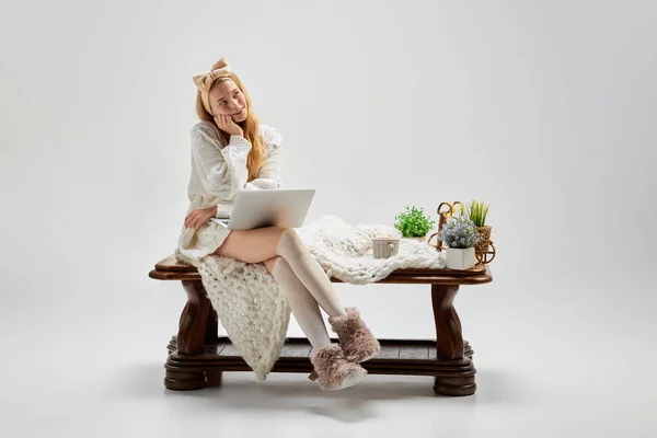 Think pleasing and positive thoughts. Beautiful dreaming girl sitting at wooden table and using laptop isolated over grey background. Ideas, inspiration, imagination. Retro, vintage style