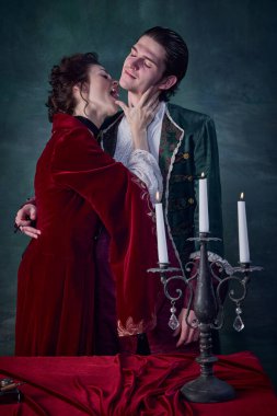 Korkunç vampir görüntüsü içindeki kadın portresi koyu yeşil arka planda genç adamı boynundan ısırıyor. Bir canavarın masum kurbanı. Cadılar Bayramı kavramı, gizem, gotik sanat, fantezi, gerçeküstü karakterler.