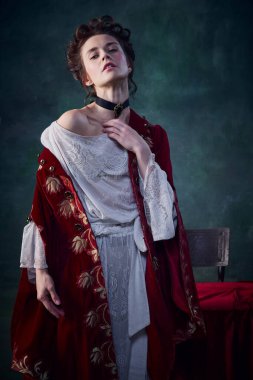 Ortaçağ elbisesi içindeki soluk tenli, koyu yeşil arka planda poz veren genç fantastik kadın portresi. Vampirlerin efsanesi. Cadılar Bayramı kavramı, gizem, gotik sanat, fantezi, gerçeküstü karakter, tarih