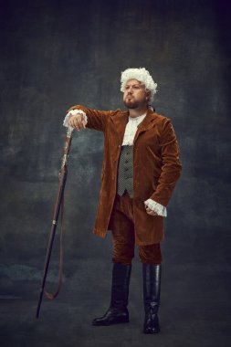 Ortaçağ 'da kraliyet avı. Eskimiş arka planda izole edilmiş eski tabancalı, eski moda avcı kıyafetlerinin yaratıcı portresi. Sanat, moda, duygular, gelenekler, hobi kavramı