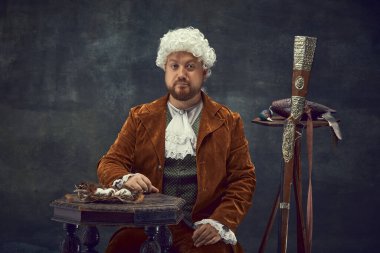 Kameraya bakıyorum. Orta çağ kraliyet avcısının koyu arkaplanda izole edilmiş beyaz peruk ve kahverengi Vintage takım elbiseli genç adamın klasik portresi. Dönem kavramlarının karşılaştırılması, Rönesans tarzı.