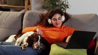 Genç kadın dizüstü bilgisayar kullanıyor ve evde İngiliz spanyel köpeğiyle yatıyor. Güzel bir kız sevgili hayvanıyla sarılıyor ve gülümseyerek bilgisayar ekranına bakıyor. Evcil hayvan konsepti