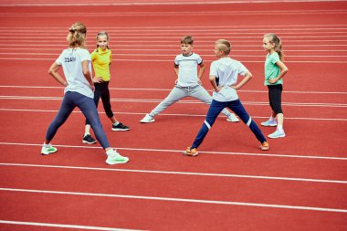 Kadın koçtan ders. Stadyumdaki koşu bandında koşmadan önce bir grup çocuk. Spor anlayışı, başarılar, eğitim, hedefler, yetenekler. Gençler spor giyim eğitiminde formda..