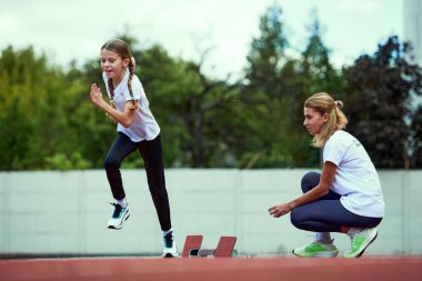 Kadın antrenör antrenörü. Stadyumda koşu bandında koşan formda bir kız. Spor anlayışı, başarılar, eğitim, hedefler, yetenekler. Spor giyim eğitimi alan küçük bir kız..