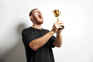 Altın kupasını tutan ve zaferi kutlayan mutlu genç erkek ya da iş adamı. Kazanan Kupalı Adam 'ın stüdyo fotoğrafı. Kazanma kavramı, başarı, insani duygular, kutlama, başarı, liderlik