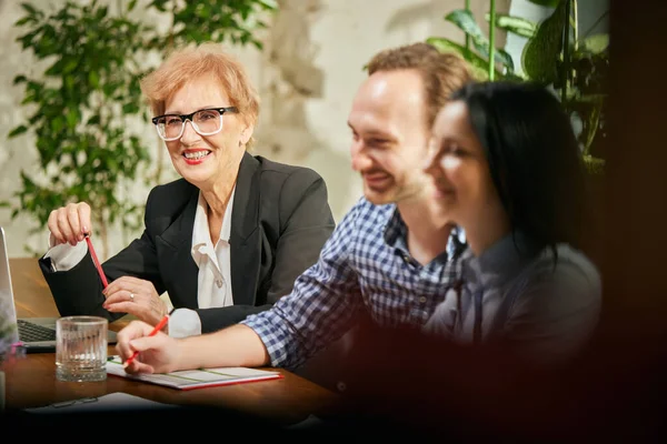 Friendly atmosphere at business gathering. Mixed ages people talking, working with colleagues at loft style office space, indoors. Business, urban lifestyle, work, finance, tech and ad concept.