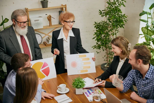 Working process, business gathering. Group of mixed ages people talking, working with colleagues, co-workers at loft style office. Business, urban lifestyle, work, finance, tech concept.