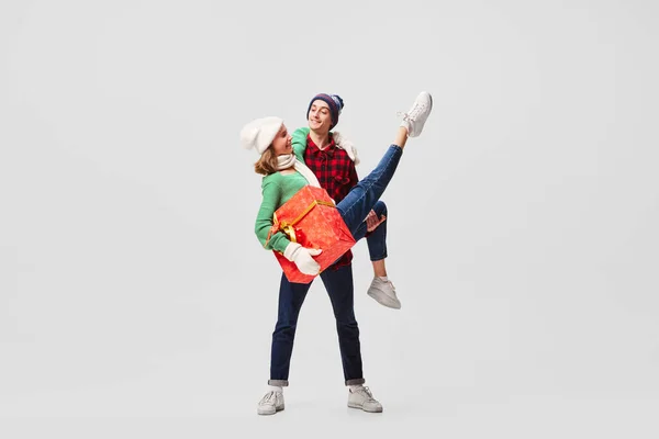 Support. Happy young people, ballet dancers in warm clothes and hats in action, motion with bright festive gift boxes on gray background. Merry Christmas, New year, holidays, 2023, party concept