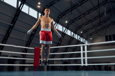 Atlıyor. Genç kaslı adam, spor salonundaki boks ringinde boksör antrenmanı. Sağlık, motivasyon ve egzersiz, spor, zorluklar, strateji. Dövüş, kas ve spor eldivenleriyle annelik stüdyosunda egzersiz..