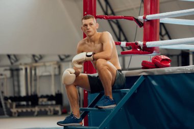 Boks ringinde sıkı çalıştıktan sonra dinlenme zamanı. Genç bir sporcu, spor salonunda spor yapmaya ara vermiş bir erkek boksör. Spor, beceri, güç kavramı.