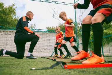 Antrenman yapıyorum. Spor stadyumunda futbol antrenmanıyla antrenman yapan genç bir futbol takımı. Küçük çocuklar, siyah turuncu futbol takımı giymiş atletler. Spor, rekabet, öğrenim ve başarı kavramı