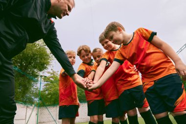 Kazanmaya kararlıyım. Küçükler futbol takımı maçtan önce dışarıda el sıkışıyor. Küçük çocuklar, siyah turuncu futbol takımı giymiş atletler. Spor, rekabet, takım çalışması ve başarılar kavramı