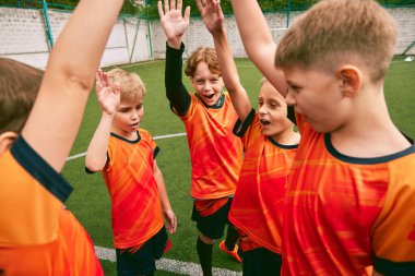 Madalyaları ve kupaları olan genç futbol takımı. Sportif çocuklar zaferi kutluyor. Futbol takımının motive çocukları el kaldırıyor. Kazanma, spor, öğrenim, başarı kavramı.