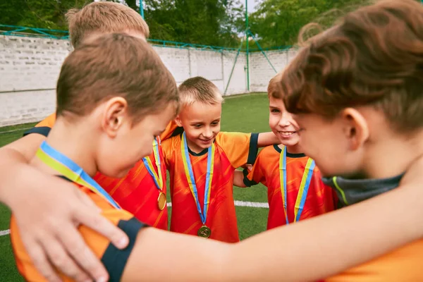 Support, motivation. Children, junior soccer team standing together in circle. Little boys, athletes in black-orange football kits. Concept of sport, competition, teamwork and achievements