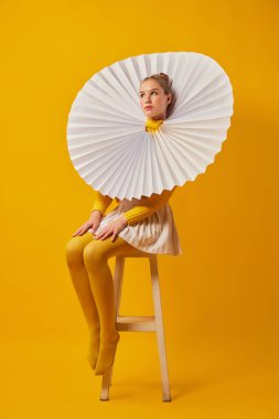 Sarı arka planda yeşil yakalı, sarı taytlı genç, kayıtsız bir kız. Modern sanat, garip güzellik, yenilikçi moda..