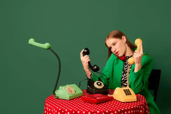 奇怪的事流行艺术 复古物品和现代青年 穿着复古风格衣服的年轻姑娘坐在餐桌旁 手里拿着老式电话 补充流行色彩 80年代 70年代风格 — 图库照片