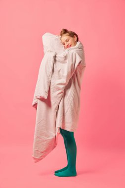 Yumuşak battaniyeye sarılı güzel bir genç kız pembe arka planda tek başına duruyor. Rahatlık, moda, sanat, yaratıcılık. Tuhaf insanlar konsepti. İlan için alanı kopyala