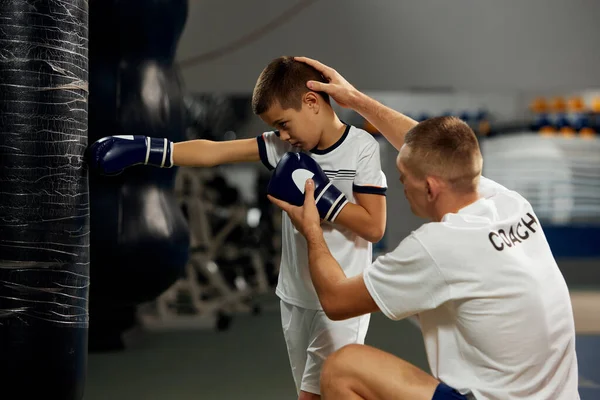 Training in boxing techniques. Junior male boxer practicing with personal coach at sports gym, indoors. Concept of studying, challenges, sport, hobbies, competition. Beginning of sports career, future