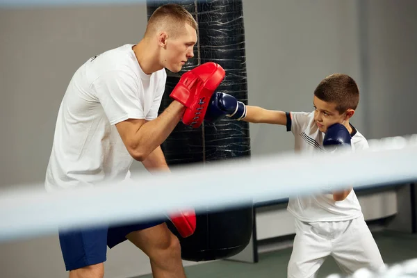 Junior athlete, male boxer training with personal coach at sports gym, indoors. Concept of studying, challenges, sport, hobbies, competition. Beginning of sports career, future champion