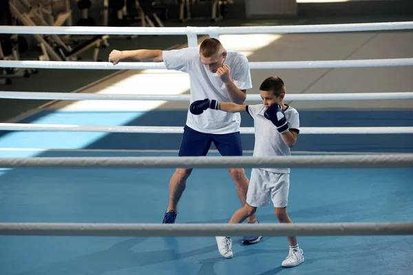 Training in boxing techniques. Junior male boxer practicing with personal coach at sports gym, indoors. Concept of studying, challenges, sport, hobbies, competition. Beginning of sports career, future