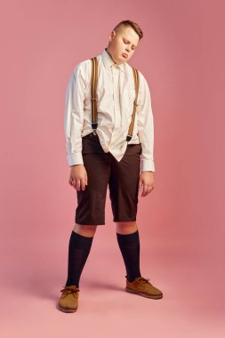Biraz kestir. Beyaz gömlekli ve şortlu, pembe arka planda izole edilmiş şişman bir gencin stüdyo fotoğrafı. Sağlık, gençlik, duygular, 70 'lerin modası, 80' lerin Amerikan tarzı.