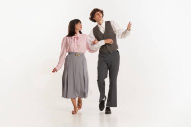 Excited young couple, stylish man and pretty woman in 70s, 80s fashion style attires walking isolated on white background. Relationships, love, care. Concept of culture, art, music, style, ad