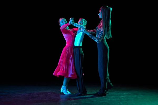 Dance class with personal coach. Two kids, school age girl and boy in black stage costumes studying to dance isolated on dark background. Art, sport dance, music, studying. Copy space for ad