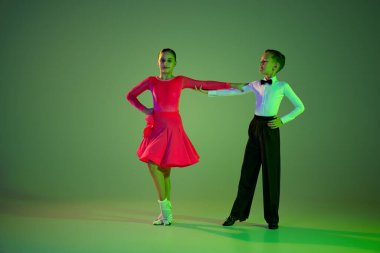 Acemi dansçılar. Yeşil arka planda, neon ışıkta izole edilmiş, dans eden güzel küçük bir kız ve erkek çocuğunun tam boy portresi. Sanat, güzellik, zarafet, eylem, duygu kavramı.
