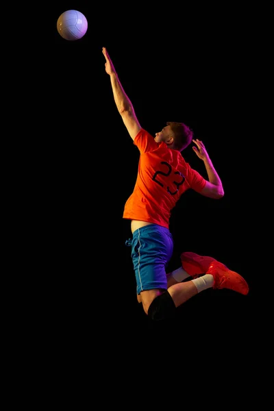 Serving. Male professional volleyball player in sports uniform training with ball isolated on dark background. Sportive man playing volleyball. Action, sport, health, team, fitness concept