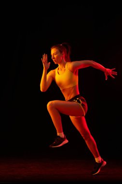 Genç sportif kadın eğitiminin portresi, karanlık arka planda neon ışıkta izole bir şekilde koşuyor. Rekabet, spor, spor, hız ve enerji konsepti. Dinamik hareketler.