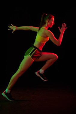 Profesyonel koşucu, koşucu neon ışıkta koyu arka planda izole edilmiş. Sağlıklı yaşam tarzı, spor, spor, hız ve enerji konsepti. Spor üniformalı ve ayakkabı eğitimli atletik kadın..
