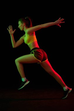 Koşu tekniği. Profesyonel bayan koşucu neon ışıkta koyu arka planda tek başına koşuyor. Sağlıklı yaşam tarzı, spor, spor, hız ve enerji konsepti. Temel hareketleri gösteren sportif kadın