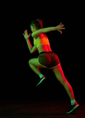 Profesyonel koşucu, koşucu neon ışıkta koyu arka planda izole edilmiş. Sağlıklı yaşam tarzı, spor, spor, hız ve enerji konsepti. Spor üniformalı ve ayakkabı eğitimli atletik kadın..