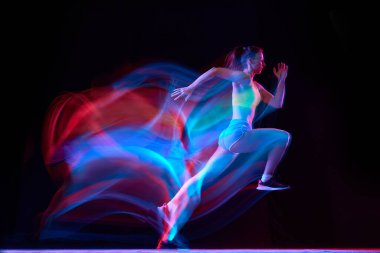 Profesyonel bayan atlet, karışık neon ışıkta karanlık arka planda koşuyor. Spor giyimli kız koşuda ya da koşuda pratik yapıyor. Sağlıklı yaşam tarzı kavramı.