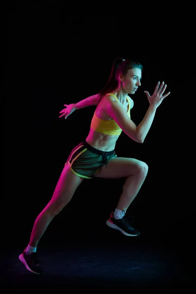 职业跑步者 跑步者在霓虹灯下在黑暗的背景下被隔离 健康的生活方式 速度和能量的概念 身穿运动服和鞋袜训练的女运动员 — 图库照片