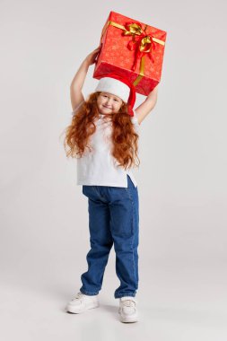Harika bir hediye. Mutlu gülen çocuk, günlük kıyafetler içinde ve Noel şapkası içinde kutular olan neşeli bir paket. Kız tatilde sevinir. Mutlu Noeller, yeni yıl. Duygular, hayaller, mutlu çocukluk kavramı