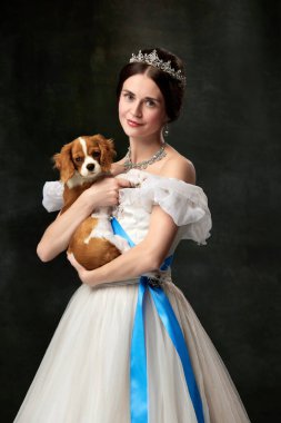Sevgili hayvanım. Beyaz klasik elbiseli çekici bir kadının portresi. Orta çağ prensesi gibi. Karanlık arka planda Kral Charles 'ın köpeğini tutuyor. Güzellik, eski moda, duygular