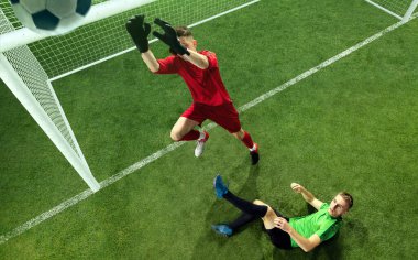 Top kale direğinin üzerinde uçuyor. Erkek futbolcu kaleci zıplayarak topu yakalıyor. Spor rekabeti, aksiyon, hareket, enerji ve dinamik konsept. Çimen alanı ve kapı 3 boyutlu.