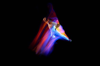 Hareket halinde dans et. Stüdyoda uçan, zıplayan dansçı veya jimnastikçinin siyah arka planda karışık neon ışınlar kullanarak havada numaralar yaptığı bir çekim. Fantezi, siber punk, spor, moda