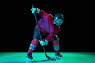 Spor üniformalı küçük buz hokeyi oyuncusu ve koruyucu ekipman neon ışıklı karanlık arka planda iş başında. Spor, güç, zorluklar, başarı, hedefler. Hokey oynayan genç çocuk.
