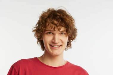 Neşeli bir bakış. Genç adamın yakın plan portresi, kırmızı tişörtlü öğrenci beyaz arka planda izole edilmiş. Duyguların kavramı, yüz ifadesi, gençlik, arzu, satış ve reklam