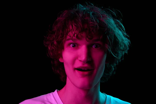 Wow, shock, surprise. Closeup portrait of young man, student in white tee isolated on dark background in neon light. Concept of emotions, facial expression, youth, aspiration, sales and ad