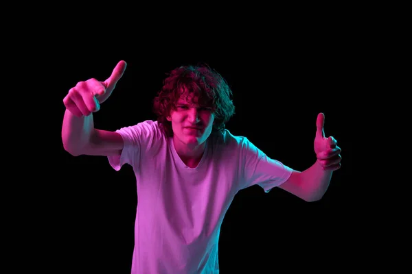 stock image Looks annoyed. Young man with discontent and undercurrent gesturing isolated over dark background in neon light. Emotions, youth, sales, ad. Model, actor wearing white cotton t-shirt