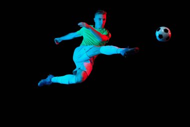 Spor iş başında. Futbol topuyla antrenman yapan profesyonel bir futbolcu koyu arka planda, neon ışık filtresiyle izole edilmiş. Spor, hız, güç ve enerji. Enerjik sporcu